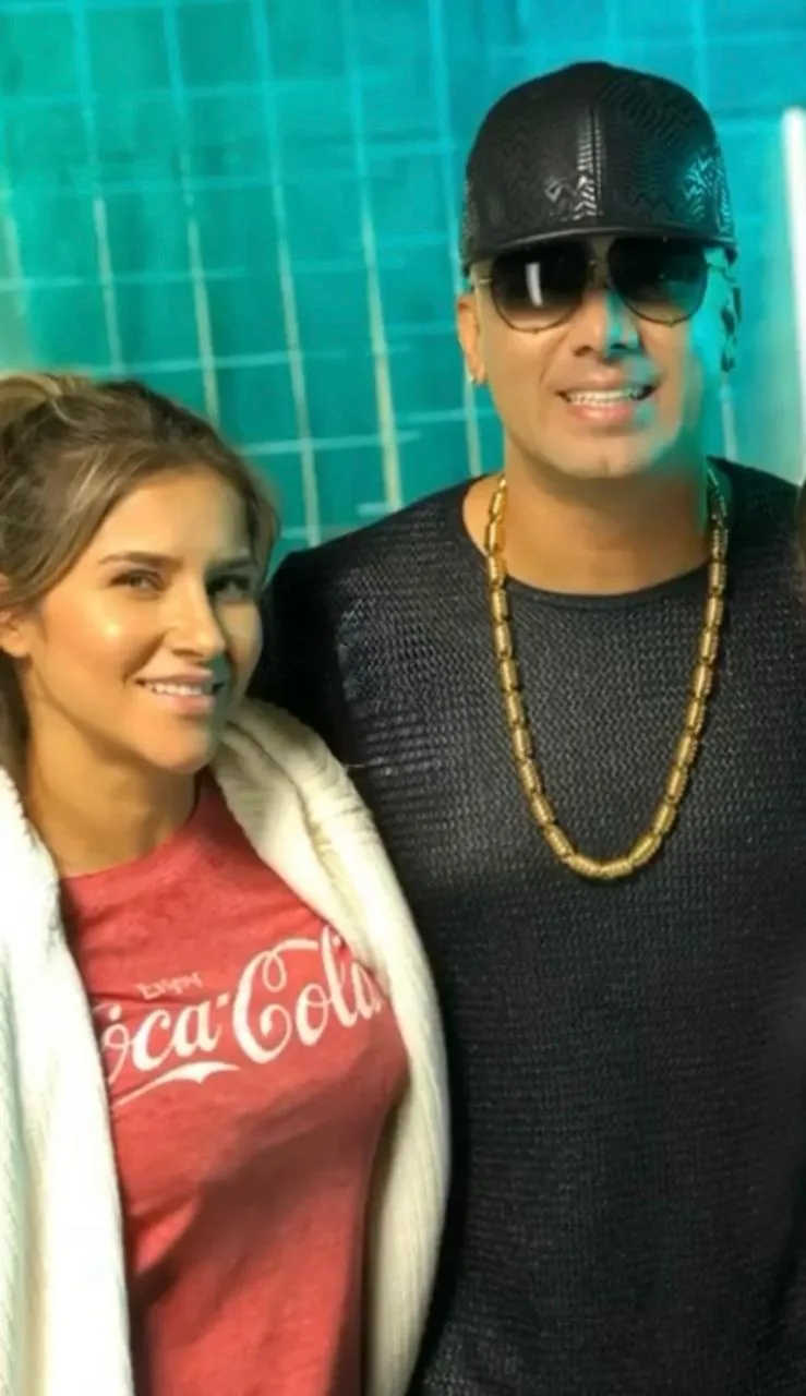 Moni Aristi junto a un artista con gorra y cadena dorada en backstage