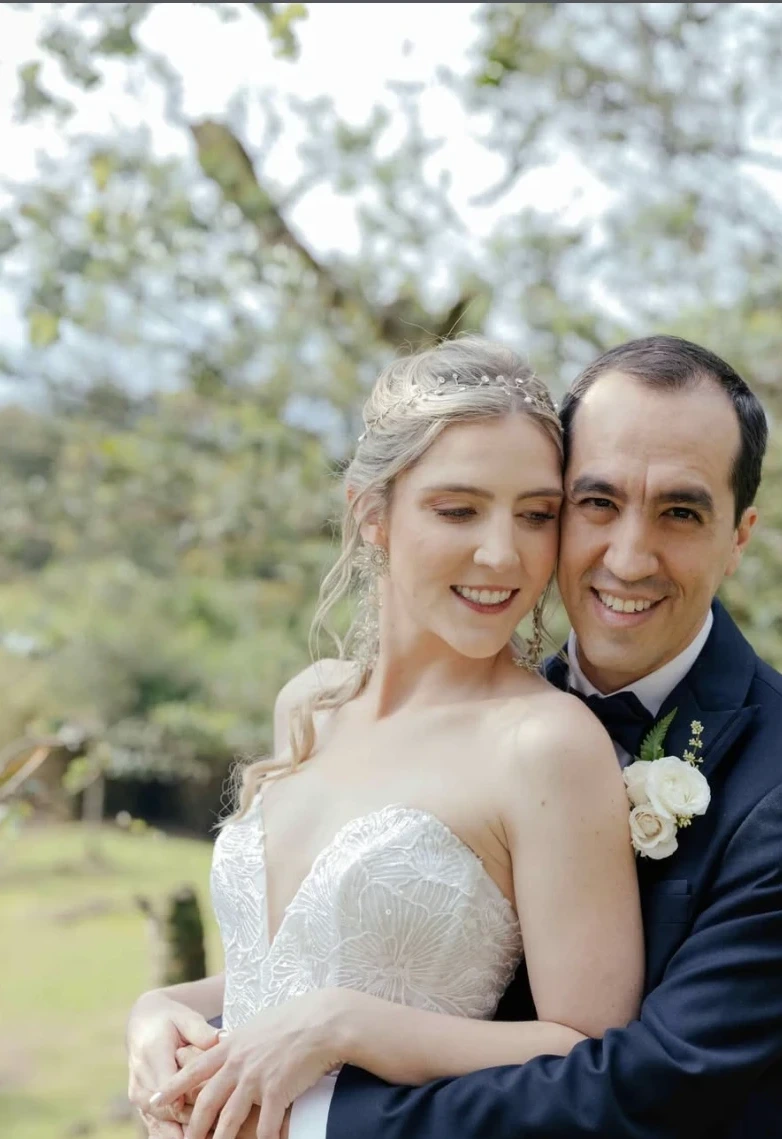 Pareja de novios abrazados en un jardín florido, novia con tocado de perlas