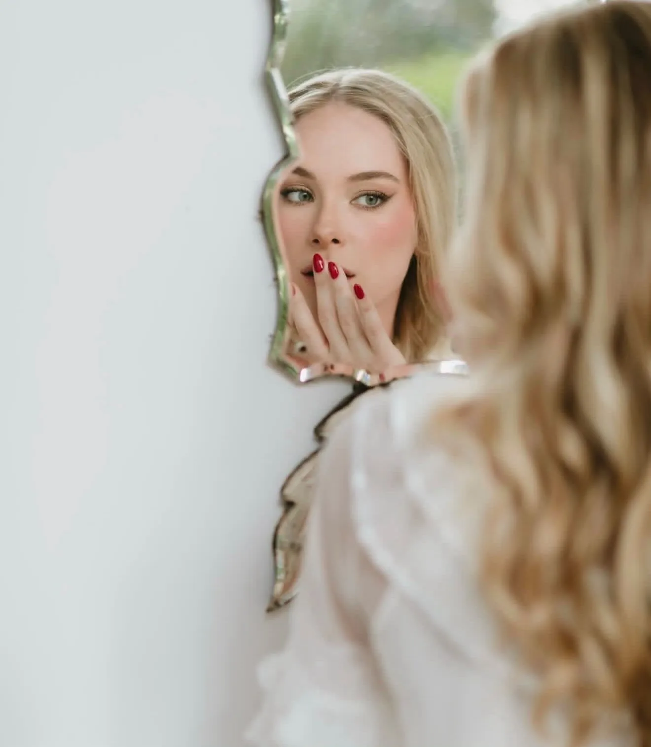 Novia mirando su reflejo en un espejo vintage, con manicura roja