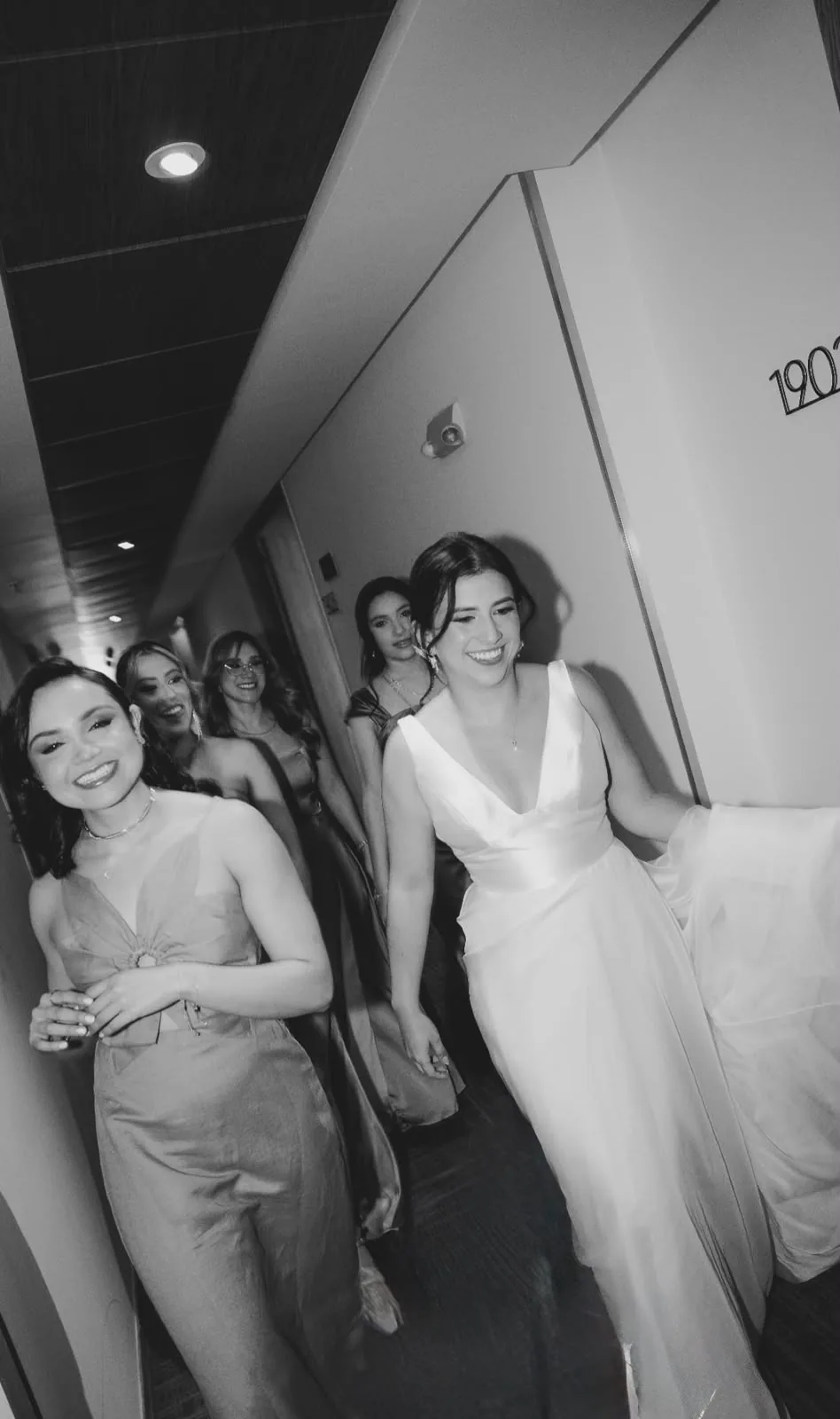Novia y sus damas de honor riendo en el pasillo del hotel antes de la ceremonia